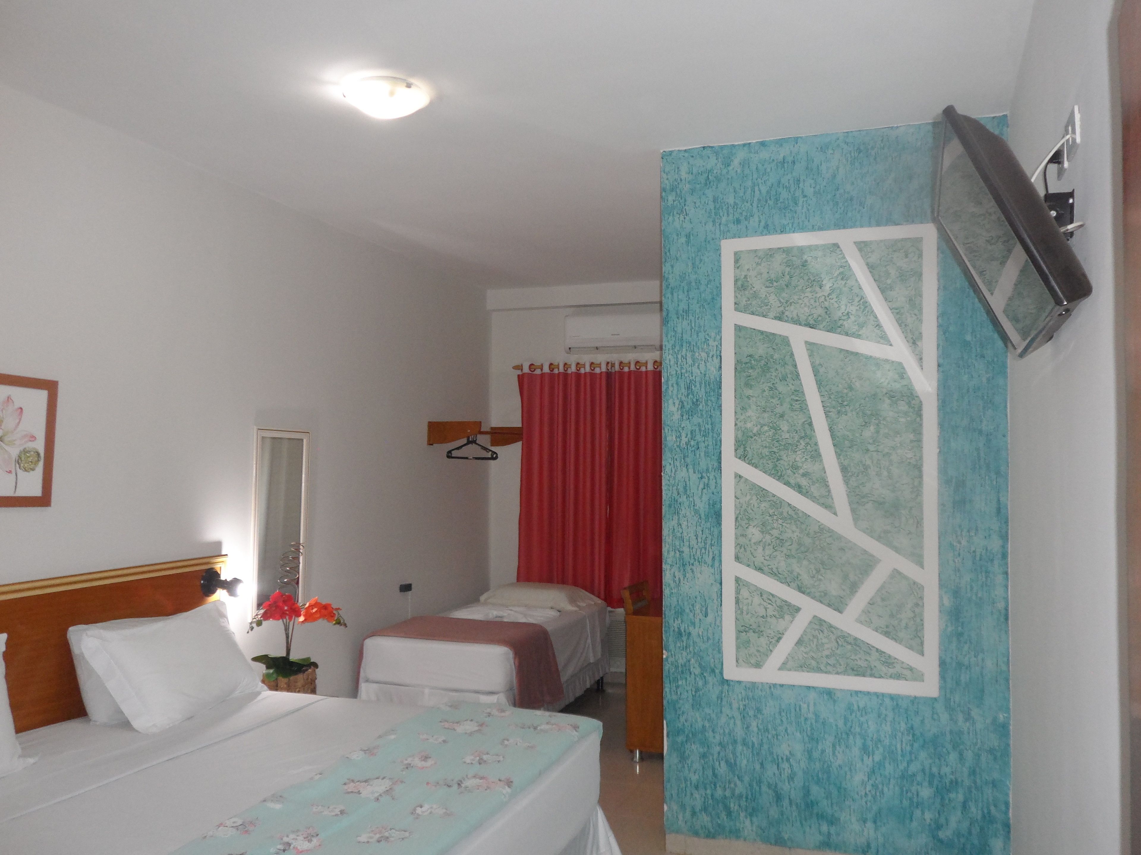 Une chambre d’hôtel avec deux lits, un miroir, un rideau rouge et un téléviseur fixé au mur.