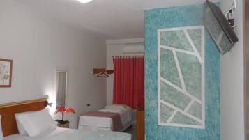 Une chambre d’hôtel avec deux lits, un miroir, un rideau rouge et un téléviseur fixé au mur.