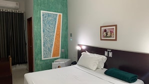 Una habitación de hotel con una cama, una mesita de noche, un aire acondicionado instalado en la pared, un cuadro enmarcado y una toalla verde sobre la cama.