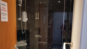 A glass-enclosed shower room with a toilet and sink, a sign requesting to close the door, and a towel rack. - Star Hotel (Montrose)