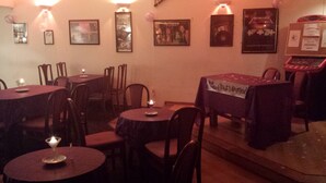 A dimly lit restaurant with round tables and chairs, framed pictures on the wall, and a small stage with a table covered in a cloth. - Star Hotel (Montrose)