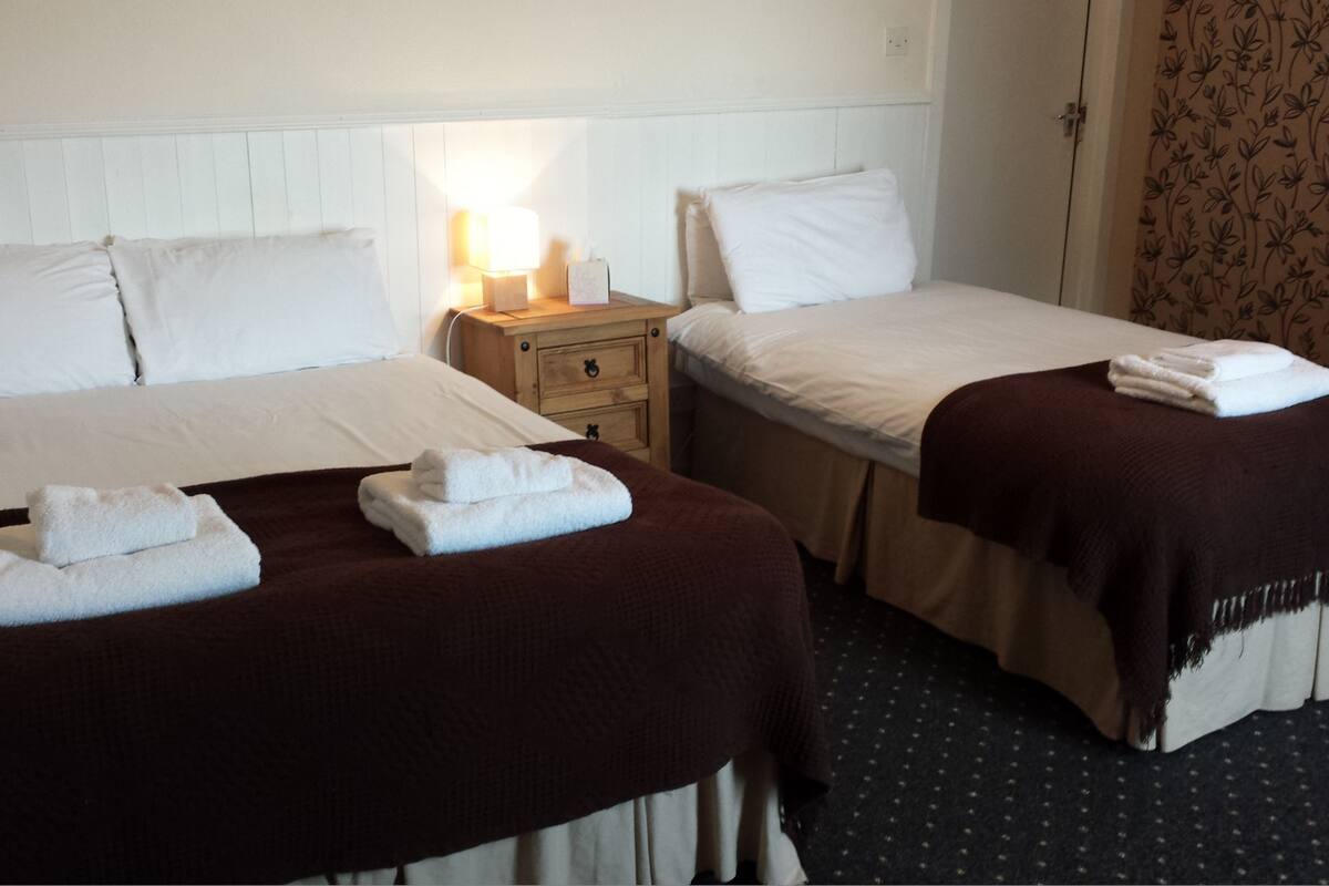A hotel room with two beds, each with white linens and a brown blanket. There is a nightstand with a lamp between the beds.