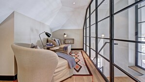 Un dormitorio tipo loft moderno con un tragaluz grande, una zona de estar acogedora con sofá y mesita auxiliar, y vistas de la ciudad a través de las ventanas.