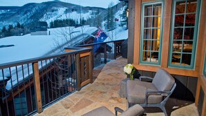 Un balcon doté d’un sol en pierre, d’une balustrade en bois et offrant une vue sur des montagnes enneigées.