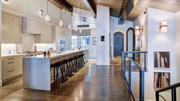 Une cuisine moderne dotée d’un îlot central, de tabourets de bar, de luminaires suspendus et d’un plafond en bois.