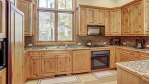 Una cocina con gabinetes de madera, encimera de granito, horno empotrado y una ventana con persianas.