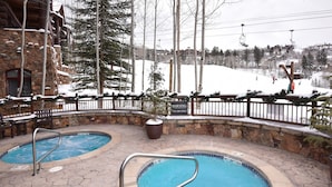 A pool area with two hot tubs surrounded by stone walls and a wooden fence.