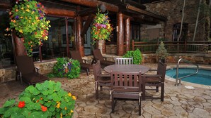 An outdoor patio with a stone floor, wooden furniture, and hanging flower baskets.