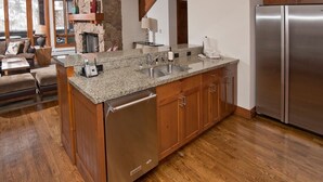 A spacious kitchen with granite countertops, a built-in dishwasher, wooden cabinets, and a stainless steel refrigerator.