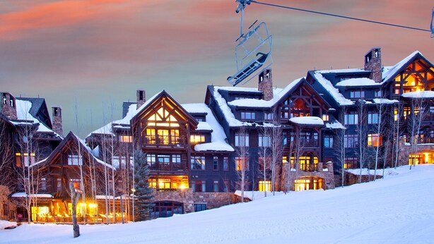 A snow-covered lodge with multiple buildings, a ski lift, and illuminated windows.