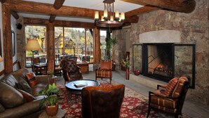 A cozy living room with a fireplace, leather sofa, and wooden chairs.