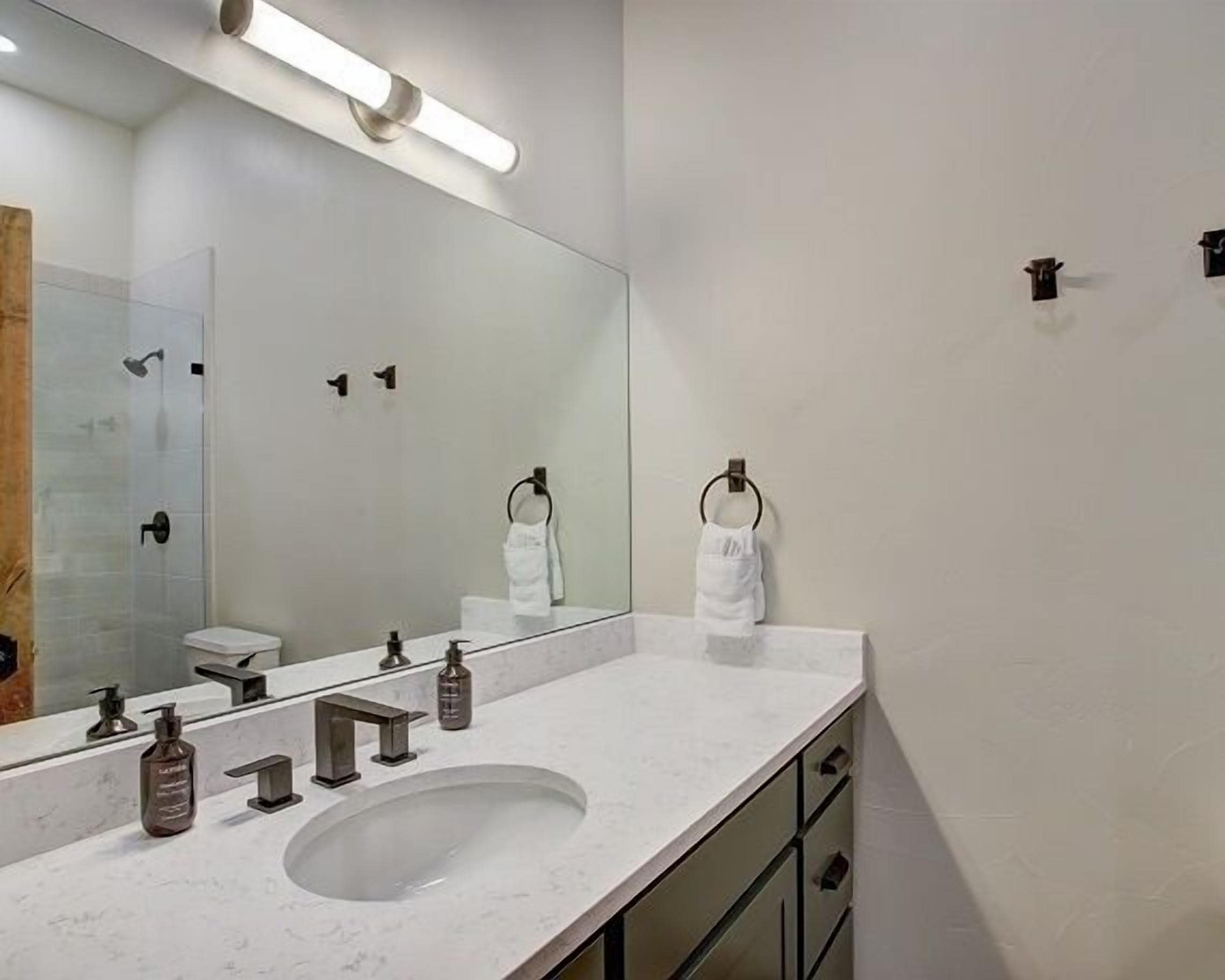 Une salle de bain moderne avec un grand miroir, un lavabo, des toilettes et un espace douche.