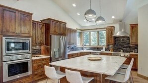 Eine moderne Küche mit Holzschränken, Edelstahlgeräten, einer großen Kochinsel mit Barhocker und einer Steinrückwand.
