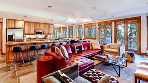 A spacious living area with a red sofa, a coffee table, and a fireplace. There is a kitchen with wooden cabinets and a large island. - Luxury 4bdr Ski In-out /premium Amenities 4 Bedroom Condo by RedAwning (Keystone)