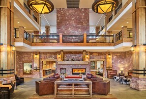 A spacious lobby with a stone fireplace, wooden furniture, and a second-floor balcony.