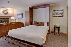 A neatly arranged bedroom with a large bed, a wooden headboard, a bedside table with a lamp, and a framed picture on the wall.