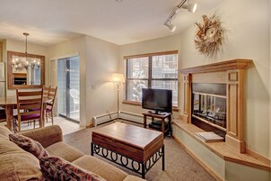 A living room with a fireplace, a television, a dining table with chairs, and a large window.
