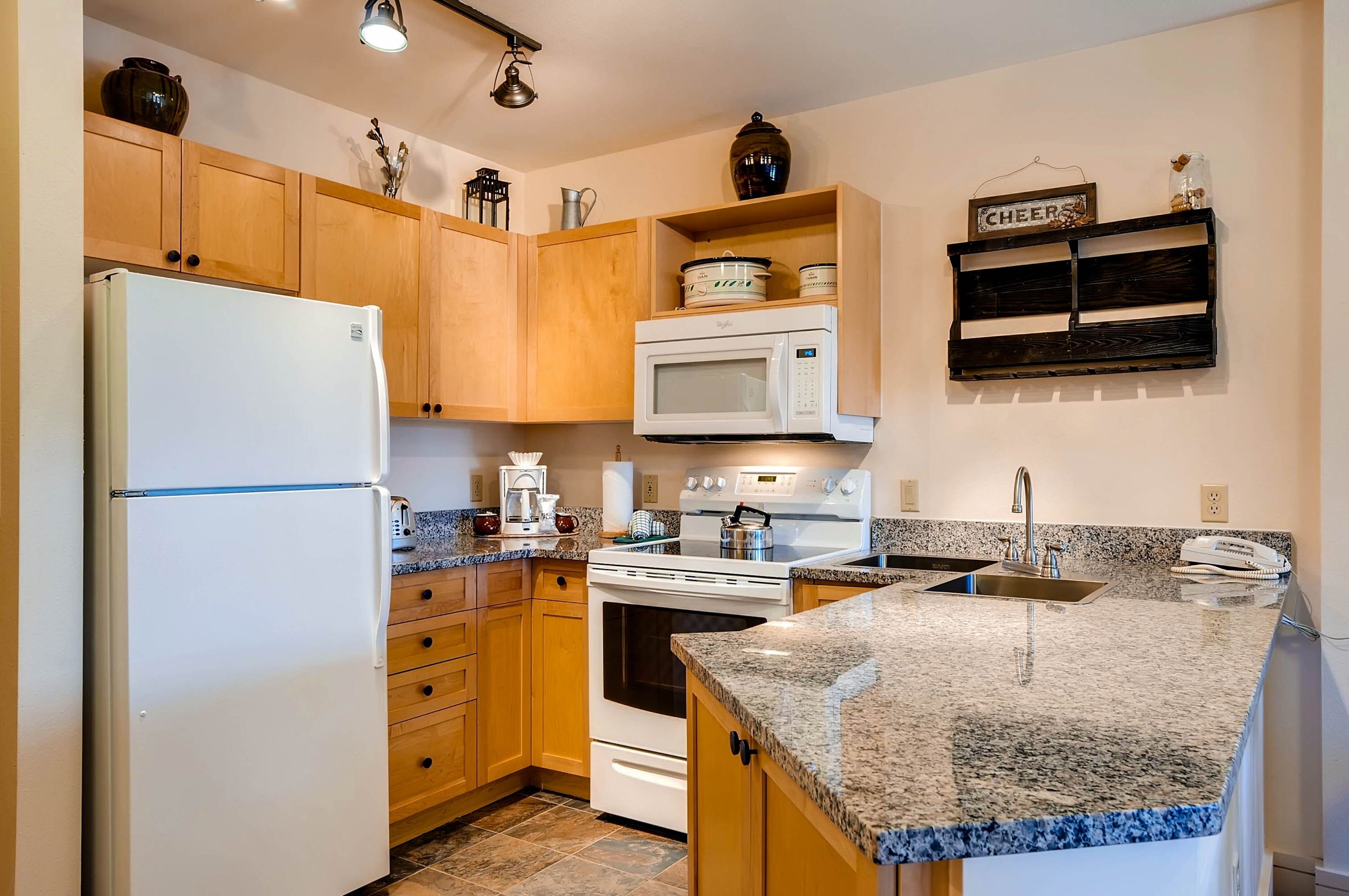 A kitchen with wooden cabinets, a white refrigerator, a microwave, a stove, and a granite countertop.