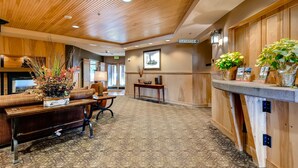 Un'ampia hall con soffitto in legno, una reception, un divano e un tavolo con un'decorazione floreale.