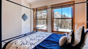 Una camera da letto con una struttura letto in metallo, un'ampia finestra con vista sulle montagne e una lampada da comodino.
