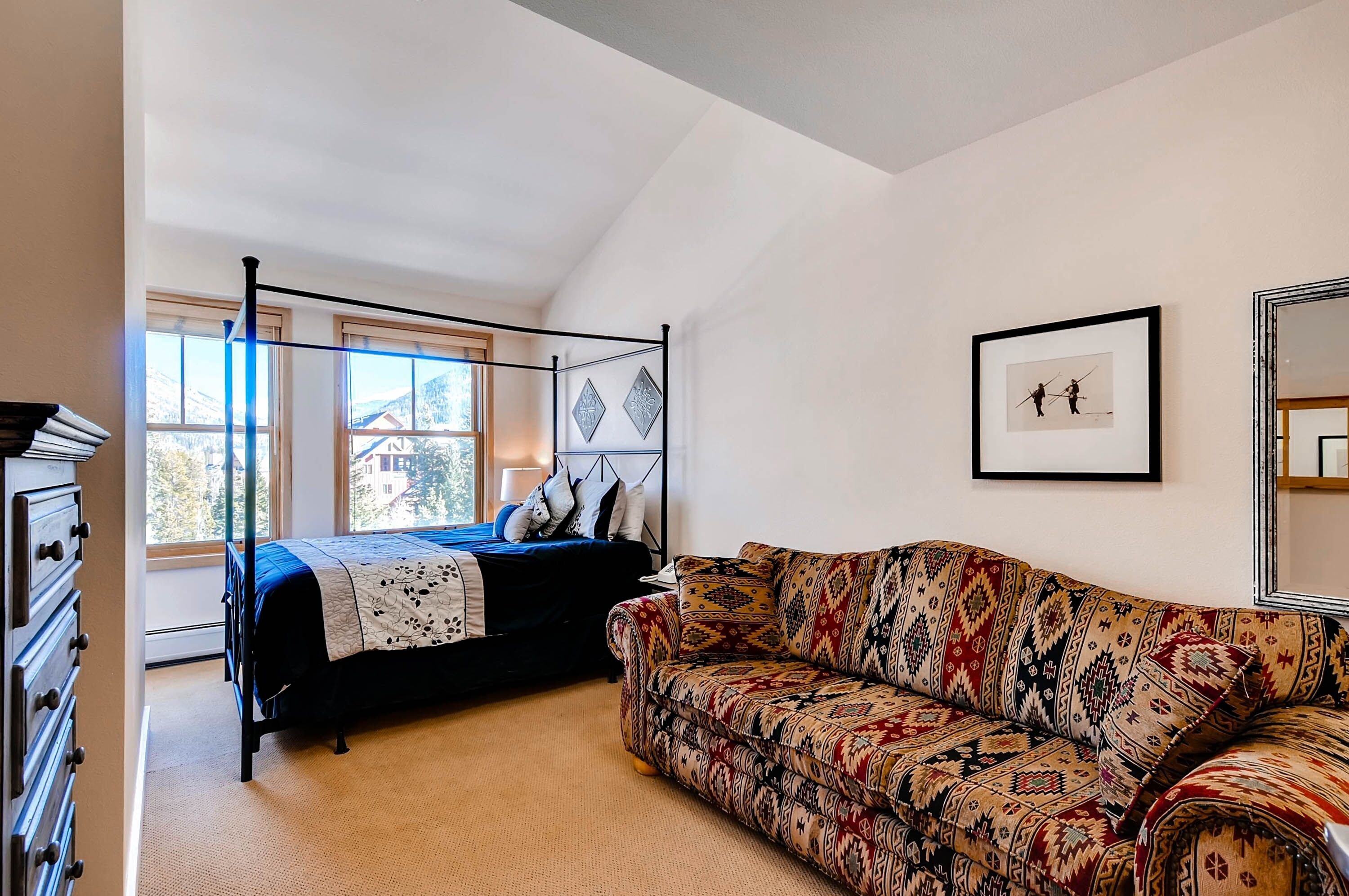 Une chambre à coucher avec un lit à baldaquin, un canapé à motifs et une grande fenêtre donnant sur des immeubles.