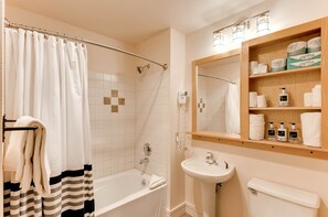A bathroom with a bathtub, a shower, a sink, and a mirror. There are towels and toiletries on the shelves. - Silver Mill 8308 (Keystone)