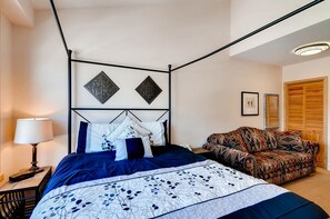 A four-poster bed with a dark blue and white floral bedspread, a patterned sofa, a bedside lamp, and a framed picture on the wall. - Silver Mill 8308 (Keystone)