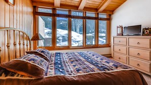 Une chambre avec un grand lit, un plafond en bois, une commode et une fenêtre donnant sur un paysage enneigé.