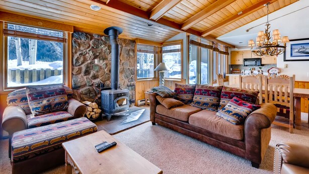 Un intérieur de chalet chaleureux avec une cheminée en pierre, des meubles en bois et de grandes fenêtres.