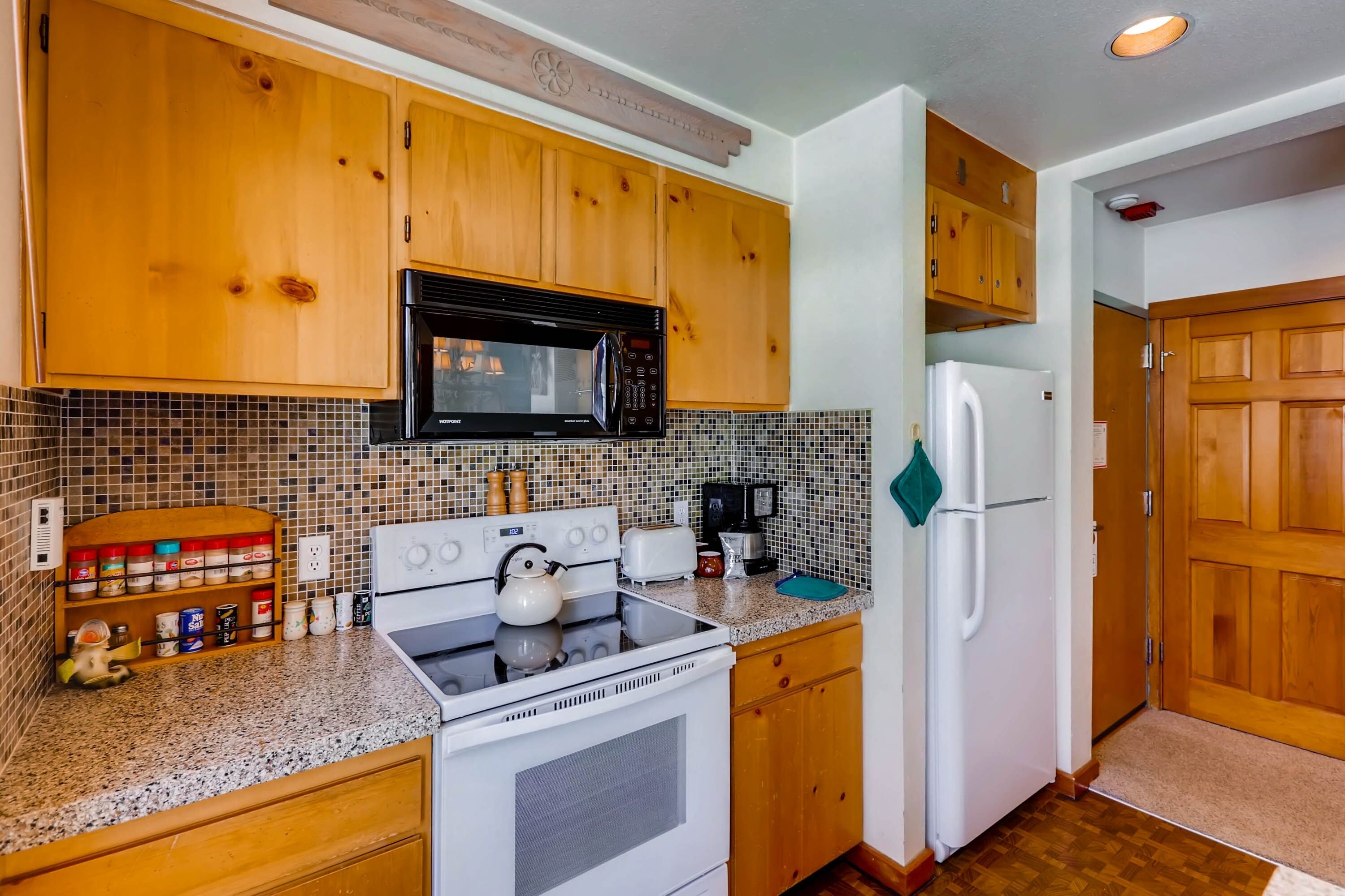 A kitchen with wooden cabinets, a microwave, a stove, a refrigerator, and a tiled backsplash.