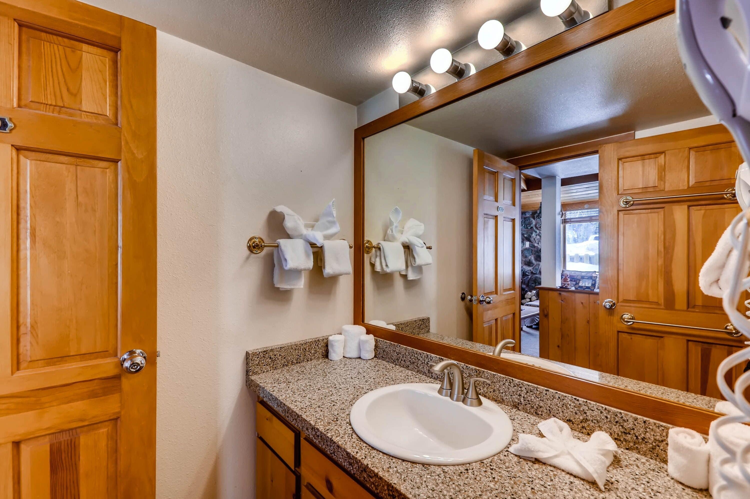 Un baño con encimera de granito, un lavabo, un espejo y puertas de madera.