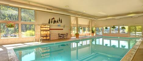 A large indoor swimming pool with clear windows, a seating area, and a wall with decorative elements.