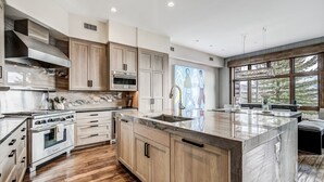 A modern kitchen with wooden cabinets, a large island, and a view of the outdoors. - Luxury renovation! Ski-in/Ski-out 5 Br Private Townhome, Top of Bachelor Gulch - majestic view & exclusive location! by RedAwning (Avon)