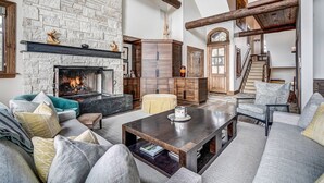 A spacious living room with a stone fireplace, wooden beams, and a staircase leading to another level. - Luxury renovation! Ski-in/Ski-out 5 Br Private Townhome, Top of Bachelor Gulch - majestic view & exclusive location! by RedAwning (Avon)