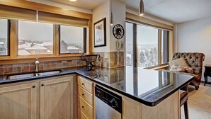 A modern kitchen with a large island, wooden cabinets, and a view of the city through large windows. - Ski-in/ski-out Studio W/snowy Alpine Views - Walk To Main St Studio Bedroom Condo by RedAwning (Breckenridge)