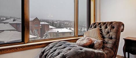 Una habitación con un ventanal grande, un sillón con capitoné y una mesita.