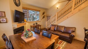 Una sala de estar acogedora con una mesa de comedor de madera, sofá de cuero y una escalera.