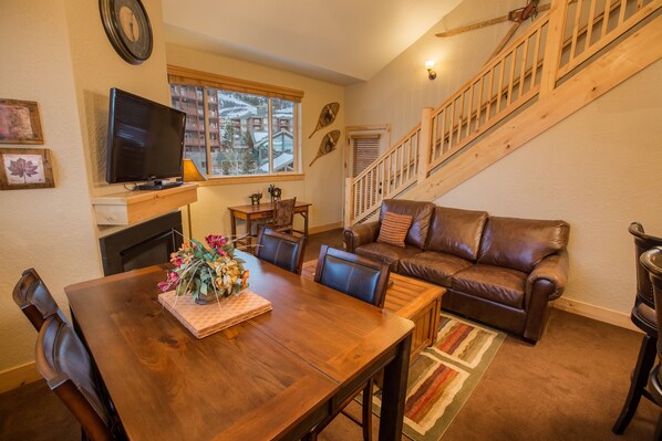 Una sala de estar acogedora con una mesa de comedor de madera, sofá de cuero y una escalera.