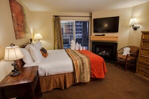 Een hotelkamer met een bed, een televisie, een open haard en een balkon met stoelen.