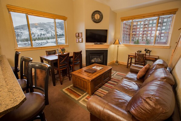 Een gezellige woonkamer met een open haard, een televisie en een groot raam met uitzicht op een besneeuwde berg.
