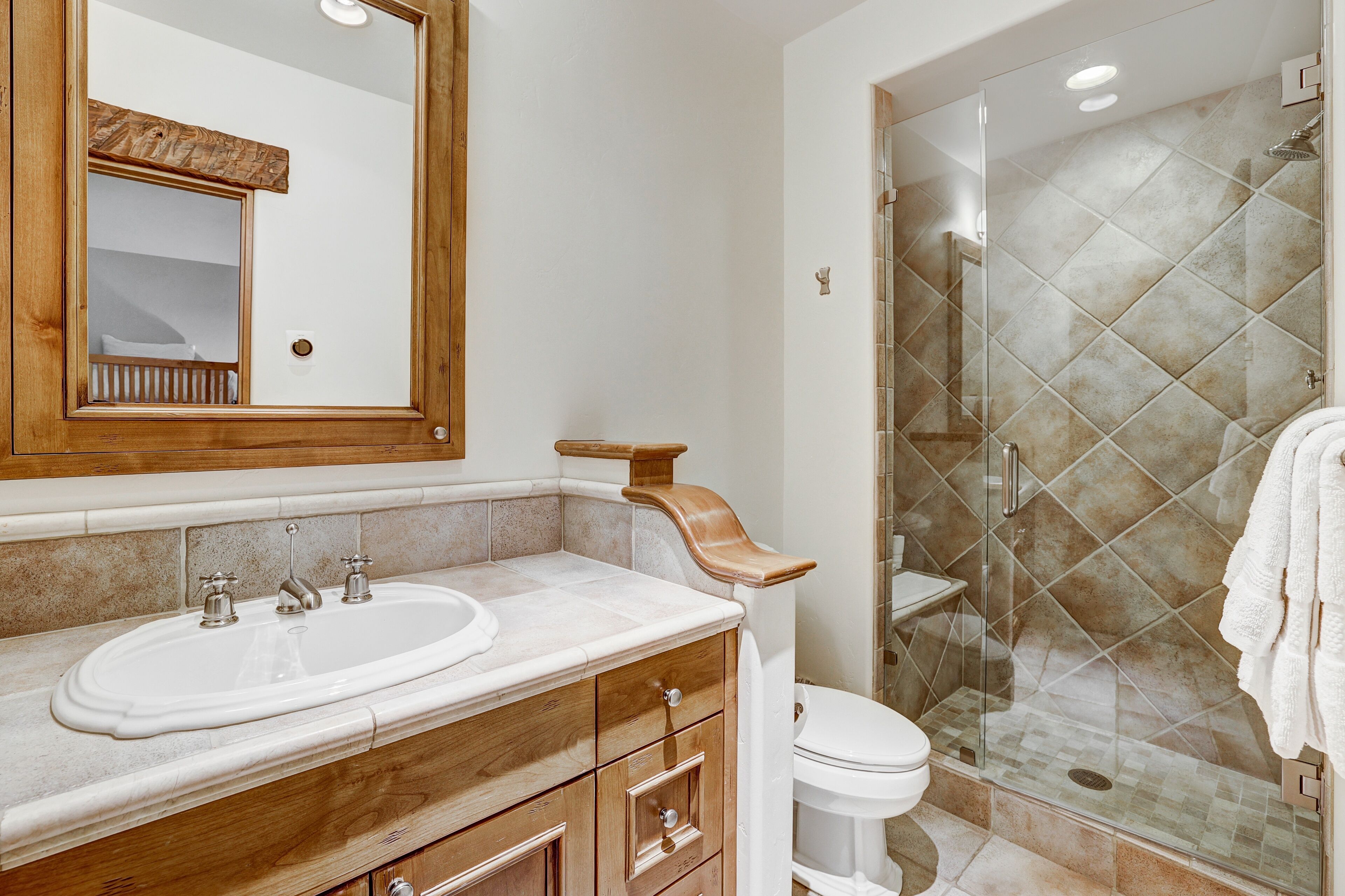 A bathroom with a wooden vanity, a large mirror, a glass shower enclosure, and a white toilet.