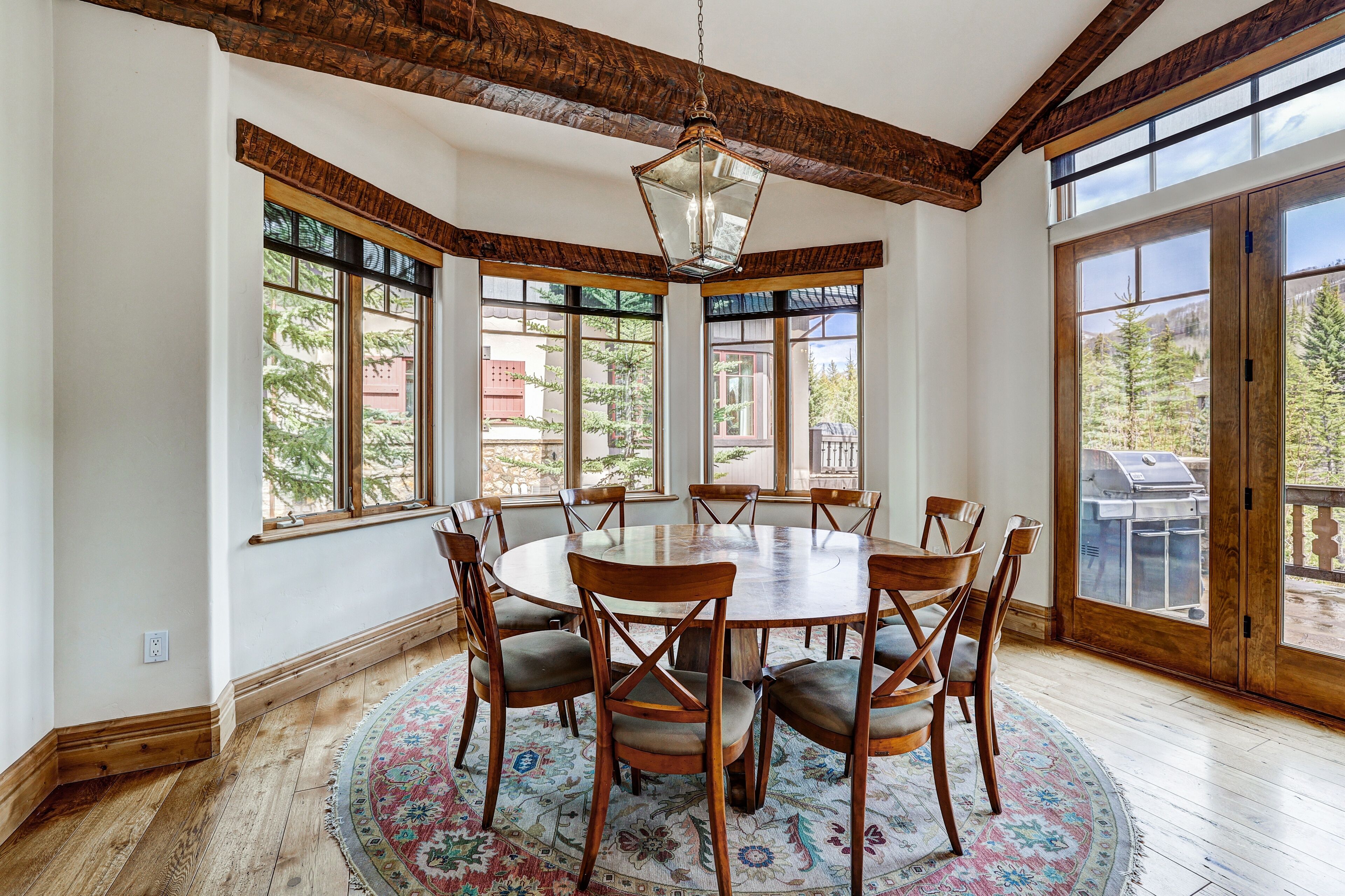 A dining room with a round table, wooden chairs, and a patterned rug.
