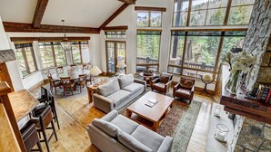 A spacious living room with a high ceiling, large windows offering mountain views, a fireplace, and a cozy seating area. - Refined 5 BR Private Home with Private Hot Tub by RedAwning (Vail)