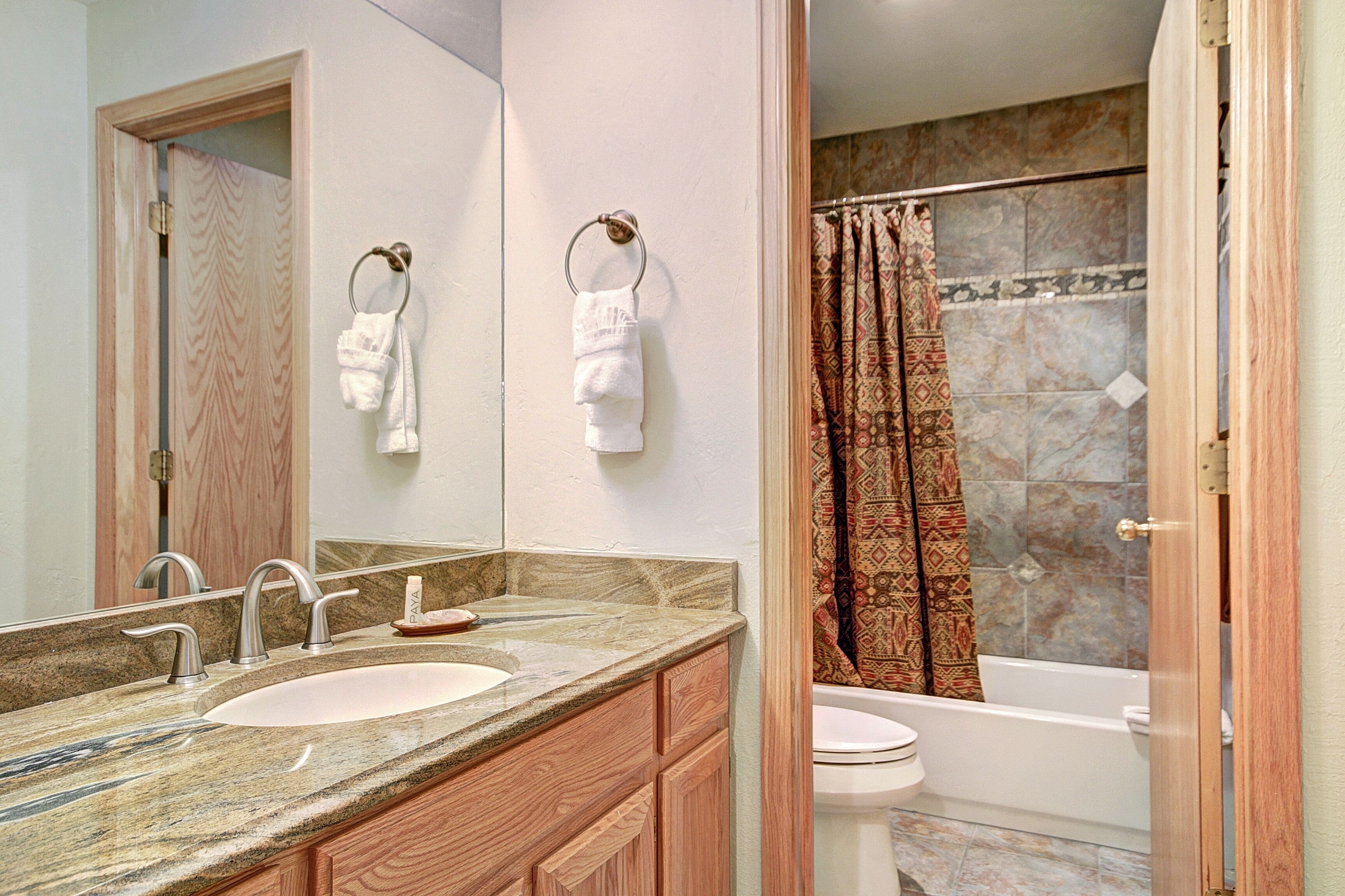 A bathroom with a sink, mirror, towel rings, and a shower curtain.