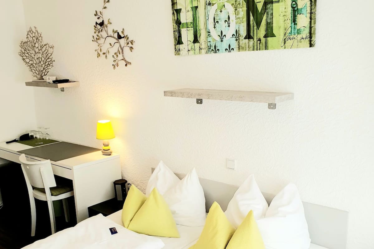 Quarto de hotel com cama, escrivaninha, cadeira, abajur e decoração na parede.