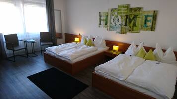 Een hotelkamer met twee bedden, een stoel, een nachtkastje en een muur met kunstwerken.