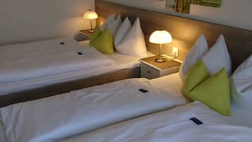 Quarto de hotel com duas camas de solteiro, cada uma com lençóis brancos e almofadas verdes. Há mesas de cabeceira com luminárias, e uma parede com a placa 'HOME'.