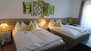 Ein Hotelzimmer mit zwei Einzelbetten, einem Nachttisch mit Lampe, einem Beistelltisch und einer Wand mit abstrakter Kunst.