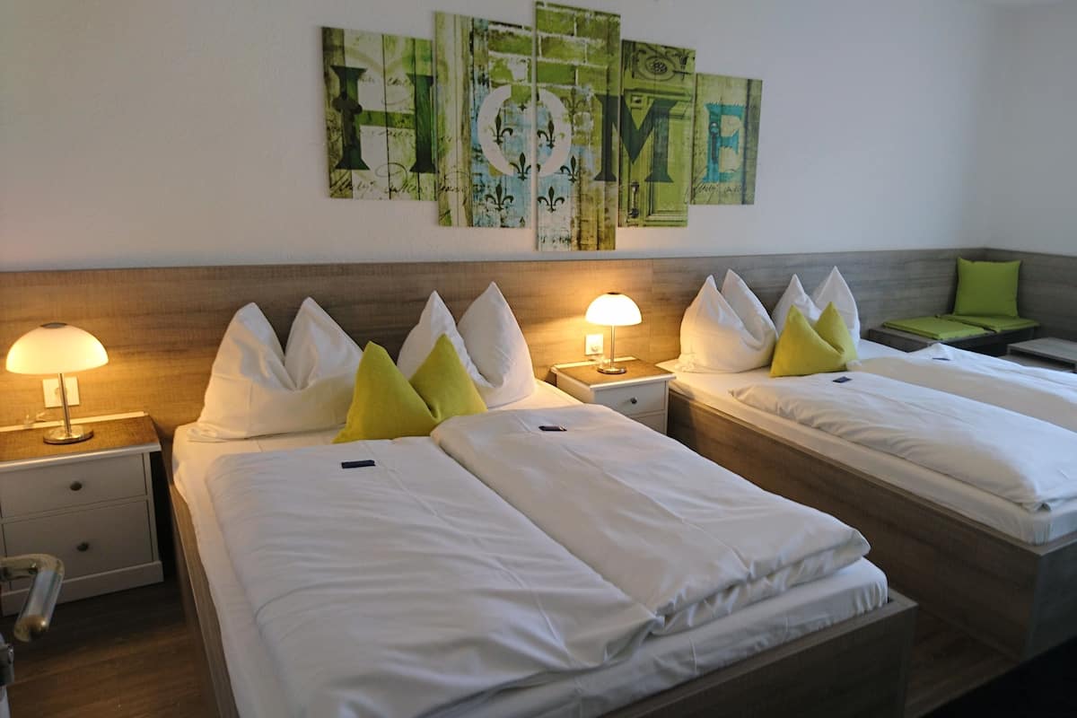 Quarto de hotel com duas camas de solteiro, mesa de cabeceira com abajur e uma parede com obra de arte abstrata.