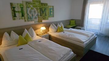 A hotel room with two beds, a nightstand with a lamp, a green chair, and a large wall art piece with the word "HOME".